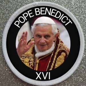 May include: A white and black circular patch with a portrait of Pope Benedict XVI. The patch has the text "Pope Benedict XVI" in a black circle with a white outline. The text "XVI" is at the bottom of the patch.