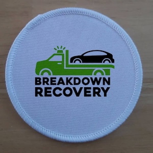 Może przedstawiać: Okrągła biała łatka z zielonym holownikiem i czarnym samochodem na niej. Tekst "BREAKDOWN RECOVERY" jest nadrukowany czarnym kolorem pod holownikiem.