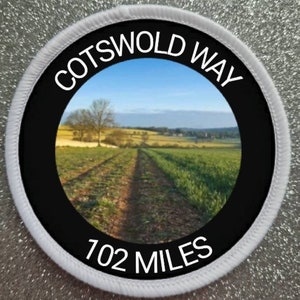 Może przedstawiać: Okrągła naszywka w kolorze białym i czarnym z napisem "Cotswold Way 102 Miles" i zdjęciem polnej drogi.