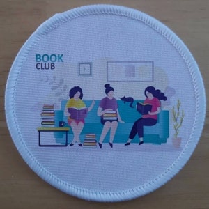May include: A white round patch with a blue couch and three people sitting on it. The people are reading books. The text "BOOK CLUB" is at the top of the patch.