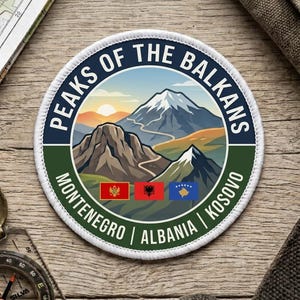 Op de afbeelding: Een ronde geborduurde patch met een berglandschap, een slingerend pad, een zonsopgang en de tekst "PEAKS OF THE BALKANS". Daaronder staan de vlaggen van Montenegro, Albanië en Kosovo met de namen van de landen in het wit.