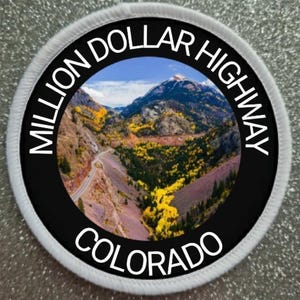 May include: A circular patch featuring a scenic mountain landscape with a winding road. The patch has the text "MILLION DOLLAR HIGHWAY COLORADO" in white lettering around the black border. The image shows a mountain range with yellow and green trees.