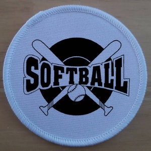 Peut inclure: Un écusson rond en tissu blanc avec des coutures noires autour du bord. L'écusson présente un graphique noir et blanc de deux bâtons de baseball croisés avec un ballon de baseball au centre. Le mot "SOFTBALL" est écrit en noir gras au-dessus des bâtons.