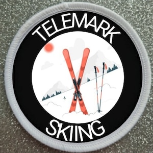 Peut inclure: Patch rond blanc avec une bordure noire et du texte blanc qui dit "Telemark Skiing". À l'intérieur du cercle, un fond blanc avec un coucher de soleil rouge, deux skis rouges croisés et deux bâtons de ski noirs.