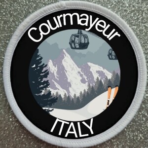 May include: A circular embroidered patch with a white border featuring a mountain landscape, two cable cars, and orange skis. The text Courmayeur is arched at the top and ITALY is printed at the bottom in white against a black background.