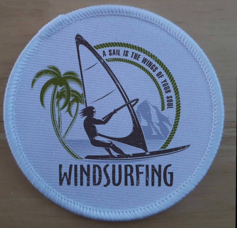 Może przedstawiać: Okrągła biała łatka z sylwetką osoby uprawiającej windsurfing. Łatka ma zielony wz&oacute;r liny z tekstem "A sail is the wings of your soul" i słowem "WINDSURFING" na dole.