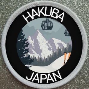 May include: A white round patch with black text and a black circle in the centre. The text says "Hakuba Japan". The circle shows a snowy mountain scene with a ski lift and skiers.