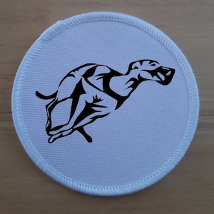 Op de afbeelding: Ronde witte stoffen patch met een zwart silhouet van een rennende windhond.