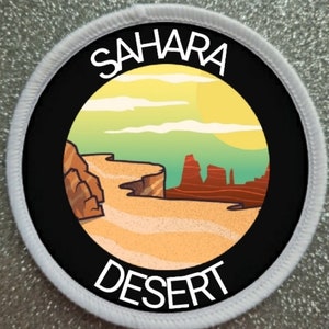 May include: A white circular patch with a black border and a colourful illustration of a desert landscape. The text "SAHARA DESERT" is printed in white on the patch.