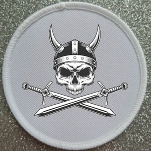 May include: A white round patch with a black and white illustration of a skull wearing a horned helmet and two crossed swords.