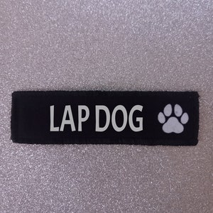 May include: Black fabric dog tag with white text that reads "LAP DOG" and a white paw print.