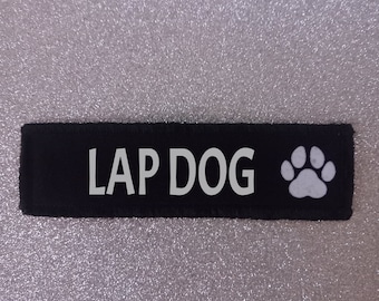 Può includere: Etichetta per cani in tessuto nero con testo bianco che recita "LAP DOG" e un'impronta di zampa bianca.