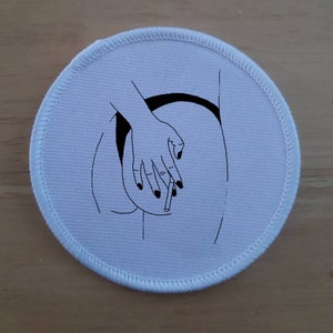 Può includere: Un cerotto rotondo bianco con un disegno a linea nera della schiena di una persona con una mano che tiene una sigaretta.