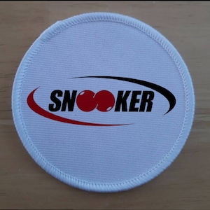 Puede incluir: Parche redondo de tela blanca con un logotipo rojo y negro que dice "SNooker" con dos bolas de billar rojas en el medio de la palabra.
