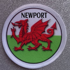 Peut inclure: Un écusson circulaire blanc avec un dragon rouge sur un fond vert et blanc. Le texte "NEWPORT" est imprimé en noir en haut de l'écusson.
