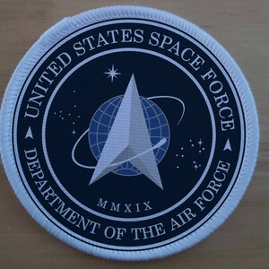 Puede incluir: Un parche bordado circular con el emblema de la United States Space Force. El diseño incluye un fondo azul oscuro, un símbolo delta plateado central, un globo terráqueo azul, estrellas blancas y el texto UNITED STATES SPACE FORCE DEPARTMENT OF THE AIR FORCE MMXIX.