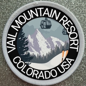 Op de afbeelding: Een ronde witte patch met zwarte tekst en een afbeelding van een besneeuwde berg met skiliften en skiërs. De tekst luidt "Vail Mountain Resort Colorado USA".