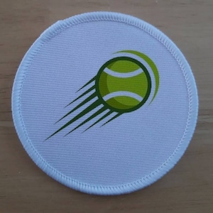 May include: White round patch with a green and yellow tennis ball design. The ball is flying through the air with a green streak behind it.