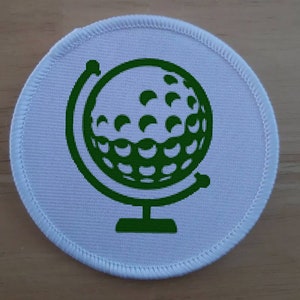 May include: A green globe with a golf ball design on a white background. The globe is on a stand.