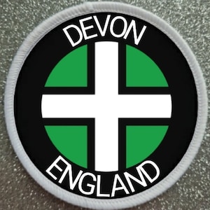 May include: A white and green circular patch with a white cross in the center. The words "DEVON" and "ENGLAND" are written in white around the edge of the patch.