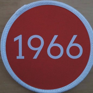 Può includere: Un cerotto circolare rosso con un bordo bianco e il numero 1966 stampato in bianco.