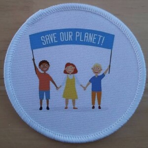 May include: A white round patch with a blue banner that reads "SAVE OUR PLANET!" Three cartoon children are holding the banner. The children are a boy with brown skin, a girl with red hair, and a boy with blonde hair.