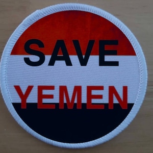 Könnte beinhalten: Ein runder weißer Aufnäher mit einem rot-weiß-schwarzen Design. Der Aufnäher trägt die Aufschrift "SAVE YEMEN".