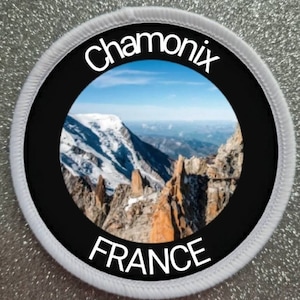 Könnte beinhalten: Runder weißer Patch mit schwarzem Rand und einem Foto einer Bergkette in der Mitte. Der Text "Chamonix FRANCE" ist in Weiß auf dem Patch gedruckt.