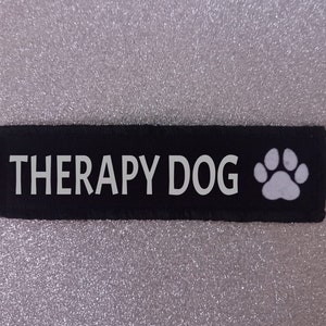 May include: Black fabric patch with white text that reads "THERAPY DOG" and a white paw print.