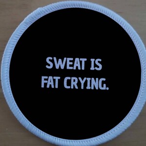 Könnte beinhalten: Ein runder weißer Patch mit schwarzem Hintergrund und weißem Text, der "Sweat is fat crying." lautet.