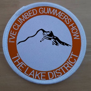 May include: A white and orange round patch with the text "I've Climbed Gummer's How The Lake District" in a circle. The patch features a black silhouette of a mountain.