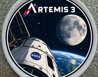 May include: A circular embroidered patch featuring a space scene with a white spacecraft, the NASA logo, and the text ARTEMIS 3. The design includes a detailed view of the moon and Earth against a dark starry background, finished with a white border.