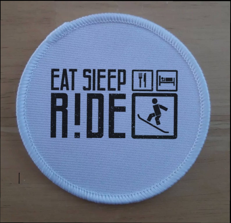 May include: White round patch with black text that reads "Eat Sleep Ride" with a fork and knife, a bed, and a skier on skis in a square.