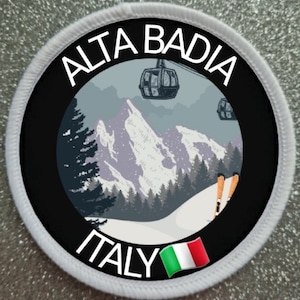 May include: A white and black circular patch with the text "ALTA BADIA ITALY" and an image of a snowy mountain scene with a gondola and skiers. The Italian flag is in the lower right corner.