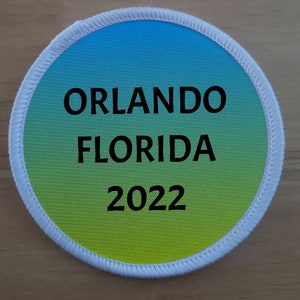 May include: A white round patch with a blue to green gradient. The text "ORLANDO FLORIDA 2022" is printed in black.