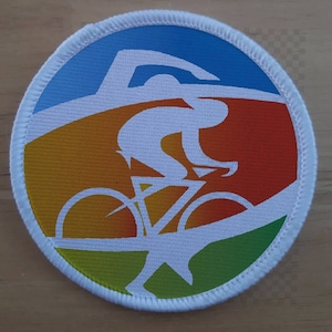 Puede incluir: Una silueta blanca de un ciclista montando una bicicleta sobre un fondo colorido. El fondo es un degradado de azul, naranja, amarillo y verde.