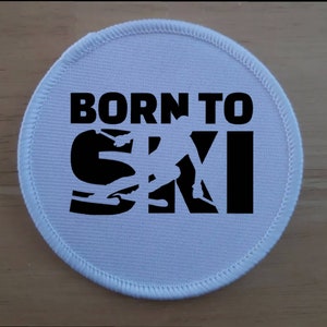 Puede incluir: Parche redondo blanco con texto negro y una silueta de esquiador. El texto dice "Born to Ski".