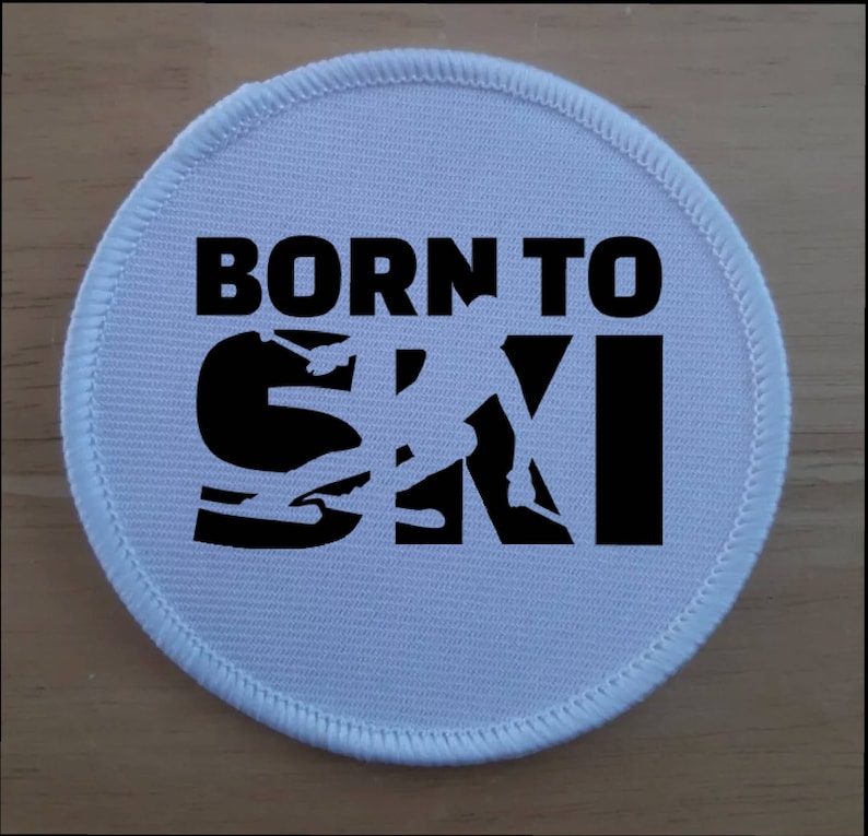 May include: White round patch with black text and a skier silhouette. The text reads "Born to Ski".