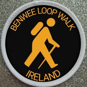 May include: A black and white circular patch with a white border. The patch features a yellow silhouette of a hiker with a backpack and walking stick. The text "BENWEE LOOP WALK IRELAND" is written in yellow around the hiker.