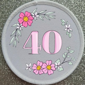 May include: A white round patch with a pink floral design and the number 40 in pink.