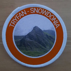 May include: A white and orange round patch with the text "TRYFAN - SNOWDONIA" in white lettering around a photo of a mountain.