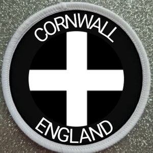 Pode incluir: Etiqueta redonda branca e preta com o texto "Cornwall England" e uma cruz branca sobre fundo preto.