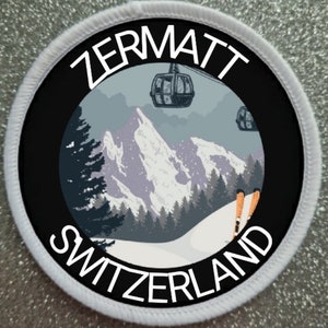 Puede incluir: Un parche redondo blanco con texto negro y un círculo negro en el centro. El texto dice "Zermatt Suiza". El círculo muestra una escena de montaña nevada con un teleférico y esquiadores.