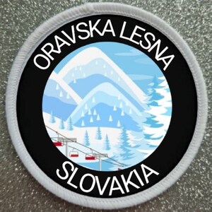 May include: Circular patch with the text "ORAVSKA LESNA SLOVAKIA" in white. The patch features a winter scene with mountains, trees, and a ski lift in shades of blue and white, set against a black background.
