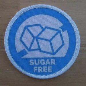 May include: A blue and white round patch with a white sugar cube graphic and the text "SUGAR FREE" in white.