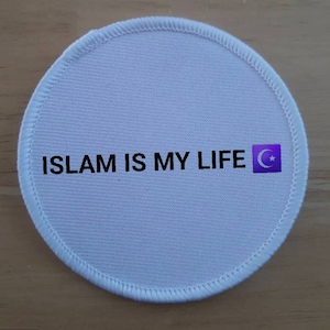 Puede incluir: Parche redondo blanco con texto negro que dice "ISLAM IS MY LIFE" y un símbolo de media luna y estrella púrpura.