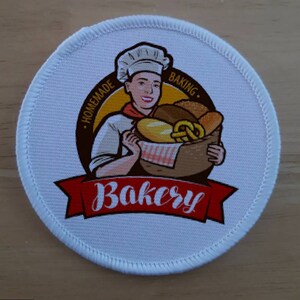 May include: A white round patch with a red, yellow, and brown illustration of a baker holding a basket of bread. The text "Homemade Baking" is in a yellow circle around the baker. The text "Bakery" is in red on a red banner.