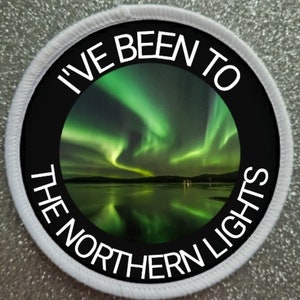Könnte beinhalten: Ein runder weißer Patch mit schwarzem Text, der "I've Been To The Northern Lights" lautet, und einem Foto der Nordlichter, die sich in einem Gewässer spiegeln.