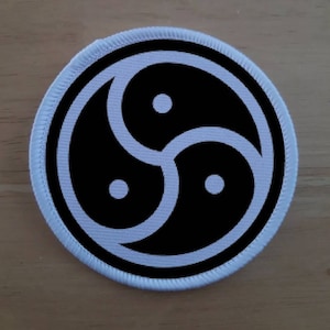 May include: A white embroidered patch with a black triquetra symbol, a three-part knot design.