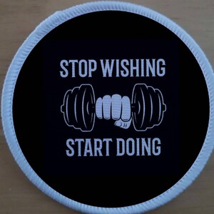 Może przedstawiać: Okrągła czarna i biała łatka z białym obramowaniem. Łatka przedstawia hantle trzymane przez dłoń i tekst "STOP WISHING START DOING".